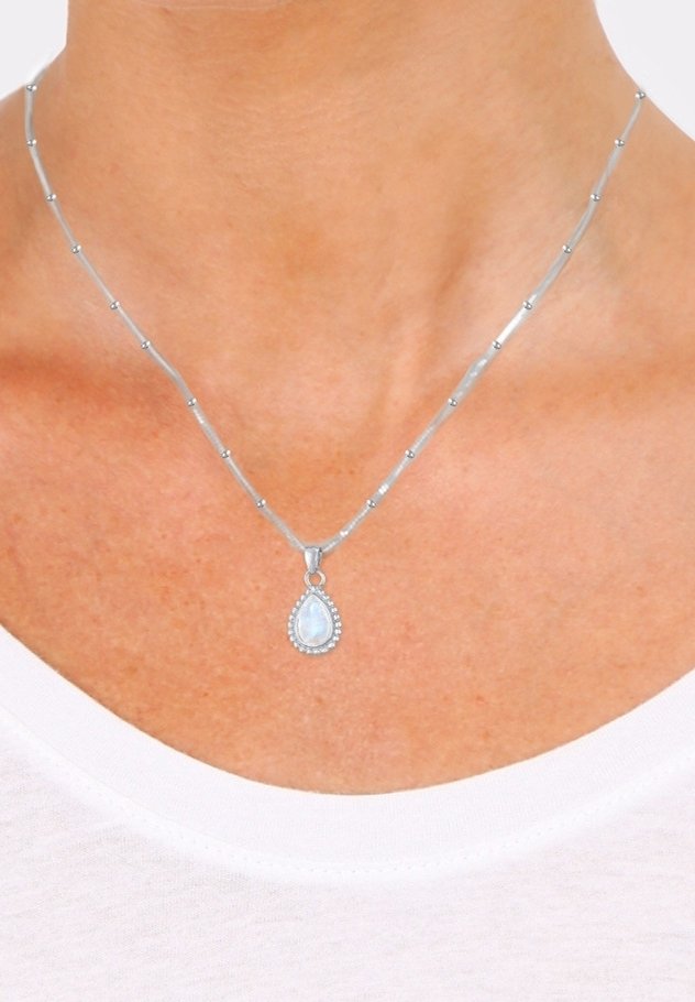 Collier en argent avec un pendentif en pierre précieuse blanche en forme de goutte porté autour du cou d'une personne, au-dessus de l'encolure d'une chemise blanche.