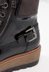 Bottine en cuir verni noir avec un panneau en suède gris, fermeture à glissière, détail de boucle métallique et semelle texturée pour une meilleure adhérence.