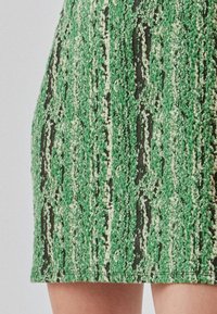 Jupe mini en tricot verte présentant un motif texturé avec des éclats blancs et un ourlet droit. Le matériau semble doux et légèrement extensible.