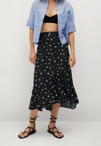 Gonna midi nera a fiori con orlo arricciato, caratterizzata da piccoli fiori bianchi e blu. Abbinata a una camicia azzurra a maniche corte con bottoni.