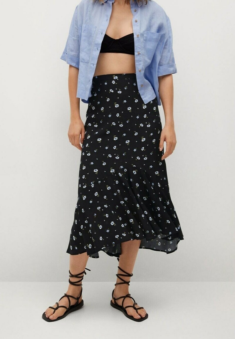 Gonna midi nera a fiori con orlo arricciato, caratterizzata da piccoli fiori bianchi e blu. Abbinata a una camicia azzurra a maniche corte con bottoni.