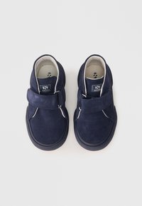 Scarpe in suede blu navy con strap in Velcro, punta rotonda e dettagli in cucitura bianca. Suole in gomma con grip testurizzato. Etichetta del marchio visibile all'interno.