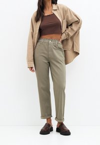 Chemise surdimensionnée beige, crop top ajusté marron, pantalon vert olive avec taille élastique, et chaussures marron à enfiler avec semelles noires.