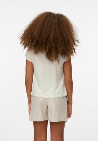 Camiseta de manga corta beige claro con un corte relajado, combinada con pantalones cortos a rayas plateadas, que presentan una textura suave y un diseño casual.