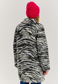 Kabát z vlnenej zmesi s čierno-bielym tigerovým pruhom, s golierom a voľným strihom, doplnený jasne ružovou čiapkou.