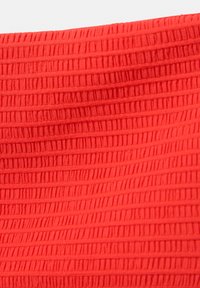 Texturiertes rotes Gewebe mit vertikalen Rillen. Das Material wirkt weich mit einem warmen Farbton und erzeugt eine haptische, gerippte Oberfläche.