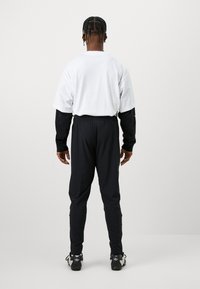 Weißes Kurzarmhemd, schwarze Langarmshirts, schwarze Hose und schwarze Sneakers. Besitzt einen entspannten Schnitt und einen elastischen Bund.