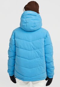 Lichtblauwe pufferjack met capuchon, voorzien van een chevron doorgestikt patroon, elastische manchetten en een logo op de achterkant. Zwarte handschoenen zijn zichtbaar.