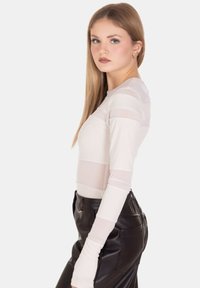 Top a maniche lunghe crema con design a righe trasparente, abbinato a pantaloni neri in ecopelle a vita alta. Tessuto liscio e stile aderente.