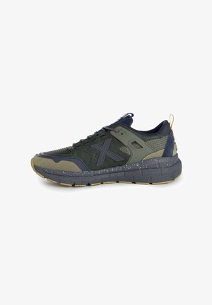 Sneaker da uomo con una tomaia in rete verde scuro, accenti blu navy, suola intermedia grigia con macchie, e una suola esterna in gomma strutturata. Presenta lacci e un piccolo manico.