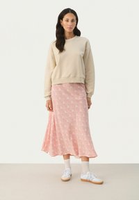 Felpa beige con polsini a costine, abbinata a una lunga gonna rosa con motivo floreale. Sneakers bianche con suola in gomma completano il look.