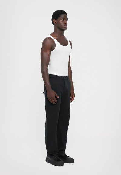 White sleeveless tank top, black wide-leg pants, and black sneakers. Fabrics appear smooth with a fitted silhouette and minimal detailing.