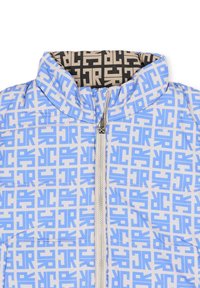 Jasnoniebieska kurtka puchowa z powtarzającym się geometrycznym wzorem w ciemniejszym niebieskim kolorze. Wysoki kołnierz i srebrny zamek błyskawiczny. Wnętrze wyściełane czarną tkaniną z jasnym wzorem.