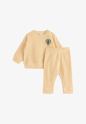 Beige langærmet top i vaffelstrik med et lille grønt luftballonpatch og matchende bukser, designet til småbørn.