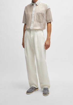 Chemise rayée à manches courtes en beige et blanc, avec une poche plaquée ; associée à un pantalon blanc taille haute ; chaussures plates grises à finition texturée.