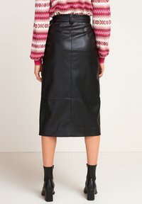 Falda midi de cuero negra con textura suave, cremallera en la parte posterior y cintura ajustada. Combinada con botas de tobillo y un suéter con estampado.