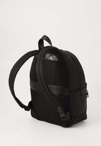 Sac à dos noir avec un corps en nylon texturé, des accents en cuir lisse, des bretelles rembourrées et un compartiment zippé.