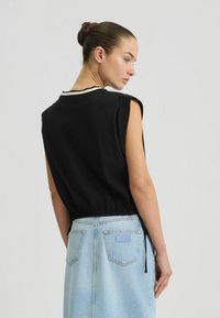 Zwarte mouwloze top met hoge hals en elastische zoom, gecombineerd met een lichtblauwe denim rok met achterzakken en een merklabel.