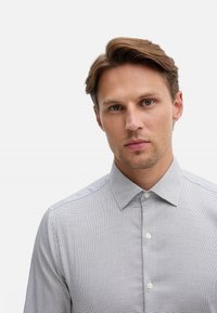 Camicia grigia chiara con bottoni, motivo a micro quadretti, collo a punta e bottoni bianchi, caratterizzata da una texture liscia e una vestibilità sartoriale.
