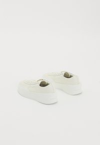 Off-white zemas sporta kurpes ar biezām baltām zolēm, ar šņorēm un smalku perforāciju, novietotas ar aizmuguri pret baltu fona.