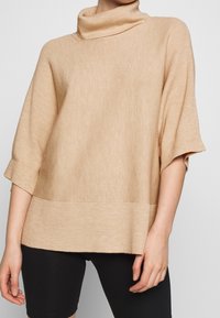 Maglione beige a collo alto a coste con maniche corte e design testurizzato, caratterizzato da un bordo inferiore uniforme e una vestibilità morbida.