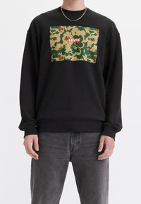 Felpa nera con un motivo camouflage in verde e beige, con un logo rosso "LEVI'S" ben visibile. Realizzata in un tessuto morbido e con maniche lunghe.
