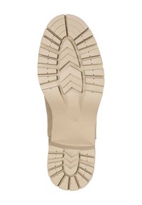 Semelle de chaussure en caoutchouc beige avec un motif de bande de roulement texturé multidirectionnel. Présente un talon arrondi et une zone centrale ovale pour l'adhérence.