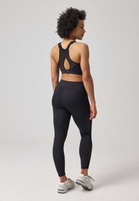Soutien-gorge de sport noir avec un dos en forme de clé et des bretelles réglables, associé à un legging noir taille haute avec des accents en maille.