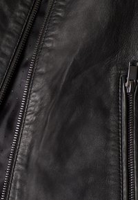 Mustassa nahkatakissa on sileä pinta, etuosassa näkyvät vetoketjuyksityiskohdat ja pehmeä sisus, jossa on pieniä reikiä.