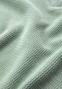 Textiel met een zachte mintgroene kleur. Heeft een ribbelpatroon met verhoogde lijnen, wat zorgt voor een luxe, fluwelige uitstraling.