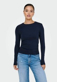 Camiseta de manga larga en color navy con escote redondo, diseño ajustado y textura suave, combinada con unos vaqueros claros con efecto desgastado.