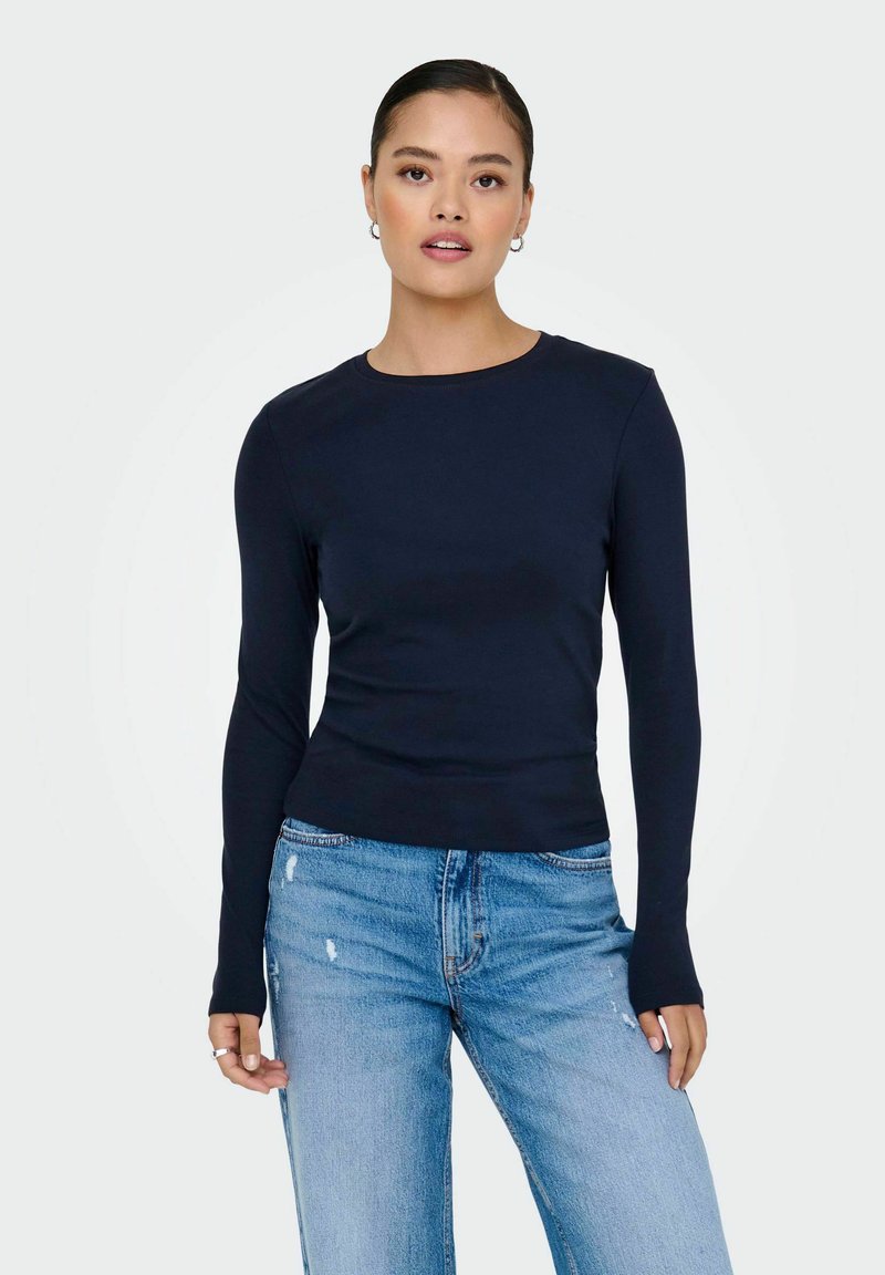 Camiseta de manga larga en color navy con escote redondo, diseño ajustado y textura suave, combinada con unos vaqueros claros con efecto desgastado.