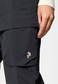 As calças de exterior pretas apresentam um tecido texturizado, um flap no bolso lateral e um logotipo bordado com um design geométrico na coxa.