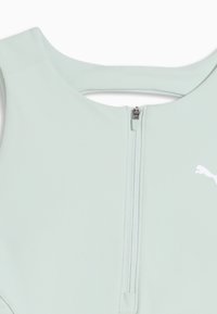 Haut sans manches vert clair avec fermeture éclair à l'avant et petit logo blanc Puma sur le côté droit près de la fermeture éclair.