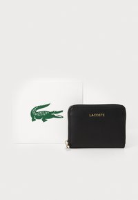 Billetera de cuero negro con el logo dorado de "LACOSTE" y detalle de cremallera, exhibida junto a una tarjeta blanca que presenta un logo de cocodrilo verde.