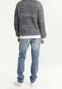 Maglione grigio a maglia con motivo testurizzato, polsini bianchi, abbinato a jeans azzurri chiari. Scarpe da ginnastica bianche completano l'outfit.