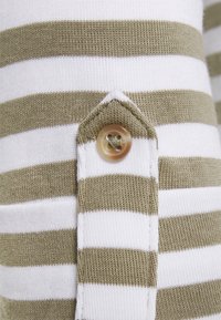 Tessuto di cotone a righe in bianco e verde oliva. Presenta una chiusura a bottoni e un'etichetta triangolare in tessuto sulla cucitura. Design a maglia testurizzata.