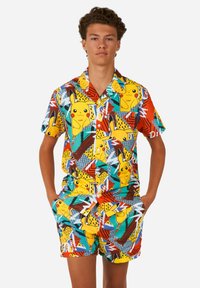 Chemise à manches courtes avec des boutons et un short assorti, avec un motif géométrique coloré et des illustrations de Pikachu en jaune, turquoise et rouge.