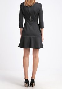 Abito nero aderente con maniche a tre quarti, gonna svasata e dettaglio con zip sul retro. Realizzato in un tessuto liscio e strutturato. Silhouette classica.