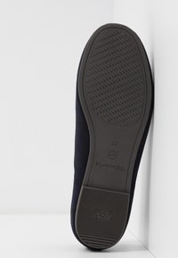 Schwarze Sohle eines Damenschuhs mit strukturiertem Profil, "Anti-Rutsch"-Griff und Größenangabe 37, die an einer weißen Kante ruht.