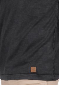Camiseta de manga corta gris oscuro con tejido texturizado. Presenta una pequeña etiqueta marrón cosida en el dobladillo. Con un ajuste simple y relajado.