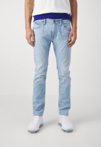 Jeans de mezclilla azul claro con corte recto, diseño de cinco bolsillos y un ligero desvanecimiento. Combinados con una camiseta blanca y zapatillas blancas.