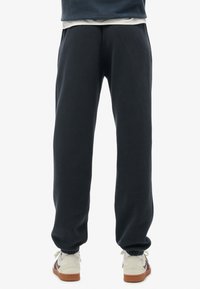 Donkerblauwe joggingsbroek van zacht materiaal, met een elastische tailleband en boorden. Gepaard met lichtgekleurde sneakers.