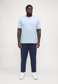 Lyseblå t-skjorte med kort erm og rund hals, kombinert med marineblå bukser og hvite sneakers. Glatt stoff med løs passform.