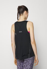 Top deportivo sin mangas negro con un panel de malla, acentos reflectantes y un corte holgado. Combinado con leggings de estampado de leopardo púrpura.