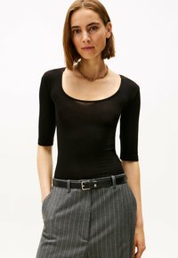 Zwarte 3/4 mouw fitted bodysuit met een ronde hals; gecombineerd met grijs gestreepte hooggetailleerde broek en een zwarte riem.