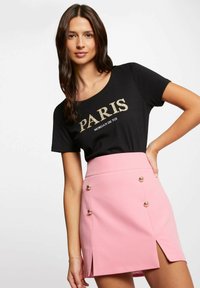 T-shirt nera con la scritta "PARIS" in stampa dorata, abbinata a una mini gonna rosa con uno spacco laterale e bottoni decorativi dorati.