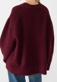 Pull oversize bordeaux avec une texture douce et duveteuse et un col rond côtelé. Le design comprend des épaules tombantes et un ourlet incurvé.