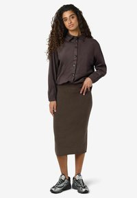 Chemise boutonnée marron à manches longues, associée à une jupe marron côtelée et des baskets grises avec des accents noirs. Design simple, sans motifs.