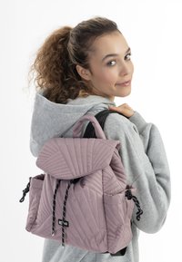 Zaino rosa trapuntato con pattina, dotato di lacci neri e tasche. Materiale morbido con un motivo geometrico sulla parte esterna.